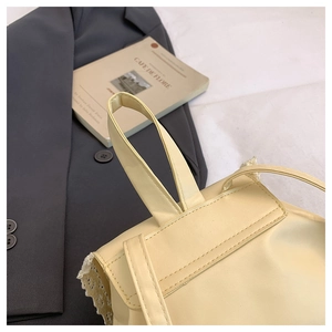 Detail of elegant beige leather handbag featuring delicate white lace trim and straps