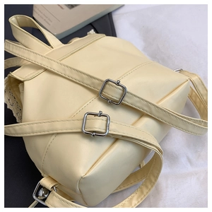 Detail of light yellow leather backpack with silver adjustable buckles and white lace trim