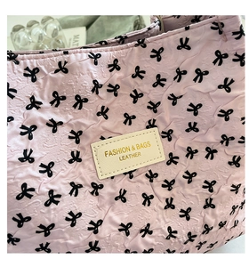 Detail of pink quilted texture handbag with black bow patterns and fashion leather tag