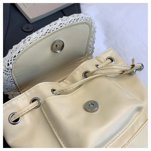 Detail view of cream PU backpack featuring lace trim, silver magnetic snap, and drawstring
