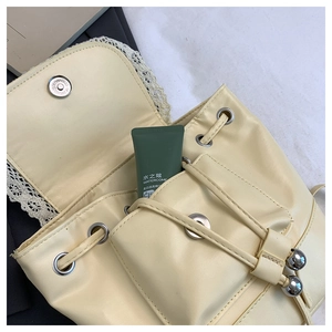 Detail of cream PU backpack featuring delicate lace trim and magnetic snap closure