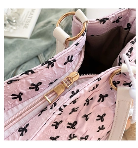 Detail of pink bow-patterned handbag showing golden zipper and pleated texture