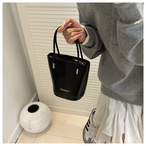 Detail of a black bucket bag featuring fashion text and polished silver metal hardware