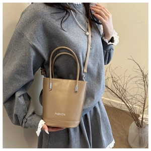 Fashion bucket bag with top handles and adjustable shoulder strap shown on a model