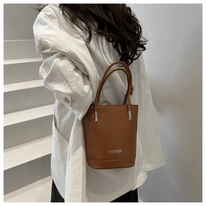 Detail of a brown leather bucket bag with silver FASHION lettering and slim handles