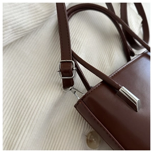 Detail of dark brown leather handbag featuring silver buckle and detachable strap