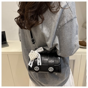 Détail d'un mini sac cylindre en cuir noir brillant avec pendentif cœur perlé et nœud