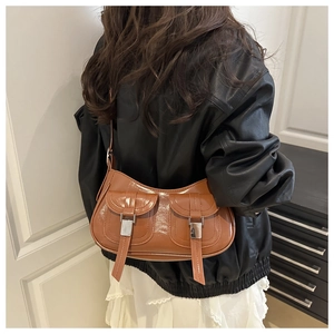 Close-up of brown faux leather shoulder bag with buckle pockets on a fashion model