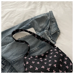 Détail d'un sac hobo noir avec motifs de nœuds roses sur fond de veste en jean