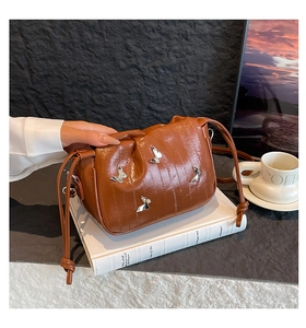 Detail of a brown bucket bag with silver butterfly charms and drawstring closure