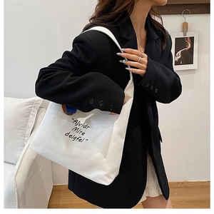 Close-up of a white canvas tote bag with black lettering worn on a shoulder