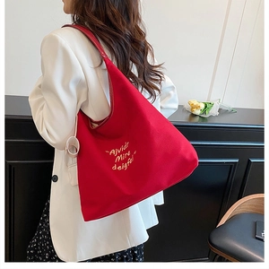 Detail of red canvas tote bag with lettering on a model in a white blazer