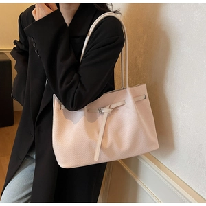 Detail of pink woven tote bag showing fine texture and metallic buckle on long shoulder strap