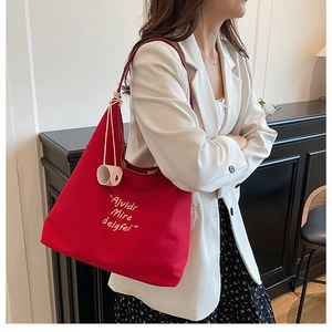 Detail of red canvas tote bag with yellow embroidery worn by a model in a white suit