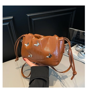 Detail of brown glossy bucket bag with silver butterfly charms and drawstring closure