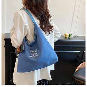 Detail of dark blue canvas tote bag with white embroidery worn by a model in suit