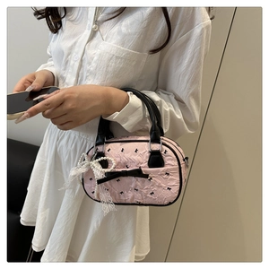 Détail d'un sac à main rose plissé avec nœuds noirs et breloque en perles dentelle