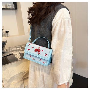 Vista dettagliata di una borsa quadrata azzurra con accenti di ciliegia 3D su una modella