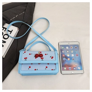 Dettaglio mini borsa azzurra con stampa ciliegie, fibbia di strass e iPad per scala