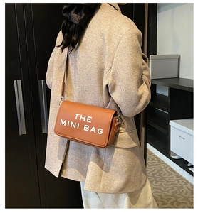 Detailed texture of brown lychee grain leather on a mini crossbody bag with white lettering