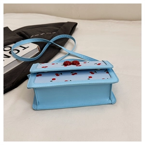 Dettaglio borsa in pelle azzurra con stampe di ciliegie e ciondolo ciliegia 3D