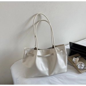 Close-up of minimalist beige leather tote bag with thin straps on a soft white surface
