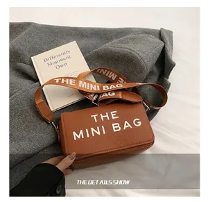 Close-up of brown pebbled leather camera bag with wide fabric strap and white letters