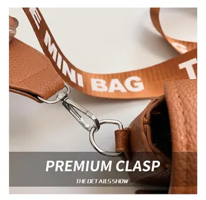 Detail of silver metal hook and textured brown leather on crossbody bag with strap