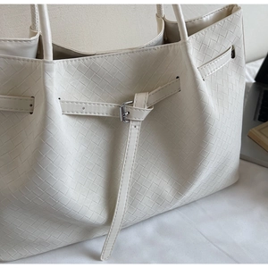 Close-up of the cream-colored woven tote bag detail showing fine texture and silver buckle