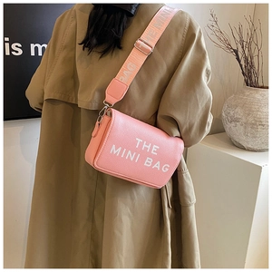 Close-up of pink mini crossbody bag with wide letter-printed strap on a model