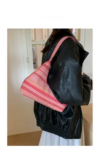 Model wearing a striped woven shoulder bag with colorful geometric raffia pattern
