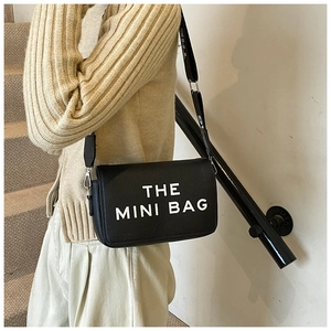 Detail of black mini crossbody bag featuring white The Mini Bag text and canvas strap