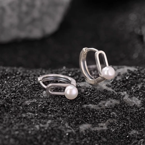 Minimalist silver oval earrings with white round pearls on textured black background