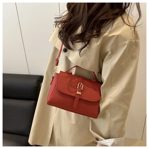 Detail of red pebbled leather handbag with gold buckle on a beige trench coat