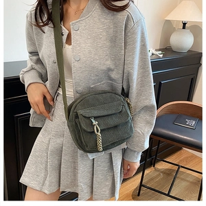 Detail of green corduroy crossbody bag featuring a front zipper pocket and woven pendant