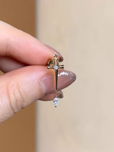 Detailed view of a golden sword stud earring with sparkling crystal embellishments