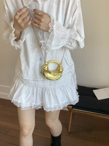 Elegant gold crescent mini handbag with round metal handle and chain strap on white lace dress