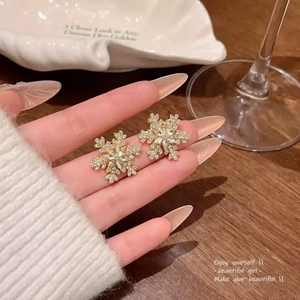 Sparkling snowflake stud earrings with crystals in gold finish held in hand