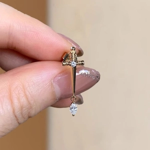 Golden cross sword stud earring with sparkling zircon held by hand to show size and detail