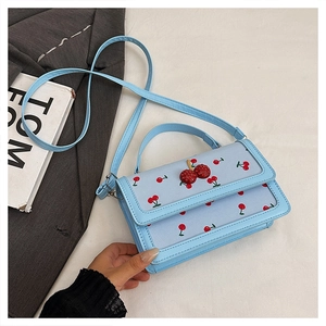Close-up of light blue handbag with cherry print and decorative 3D cherry accent