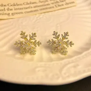 Elegant gold snowflake stud earrings with sparkling pave zircon on a white ceramic plate