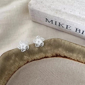 Delicate silver hollow flower stud earrings with intricate texture on a ceramic plate