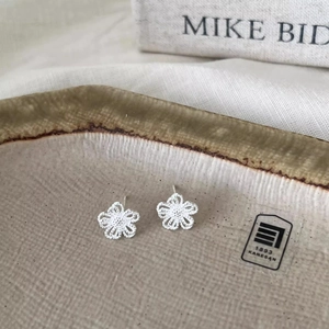 Delicate silver hollow flower stud earrings displayed on a minimalist ceramic tray