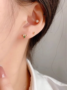 Macro shot of gold honey bee ear stud with green gemstone and small gold ball studs