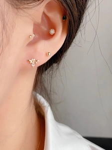 Close-up of golden bee cartilage stud with zircons and layered earrings on ear
