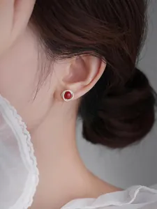 Dettaglio di orecchini vintage con gemma rossa e contorno bianco sull'orecchio femminile