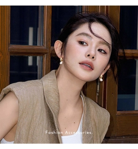 Detail of baroque pearl and golden teardrop earrings worn by a model in soft lighting