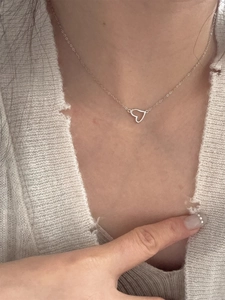Dettaglio di una collana minimalista con ciondolo a cuore argentato sulla clavicola