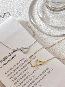 Dettaglio di collane cuore traforate minimaliste in oro e argento su carta testurizzata