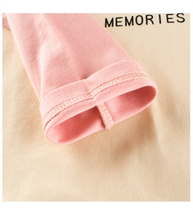 Dettaglio dei polsini rosa e stampa Memories su una maglietta beige a maniche lunghe